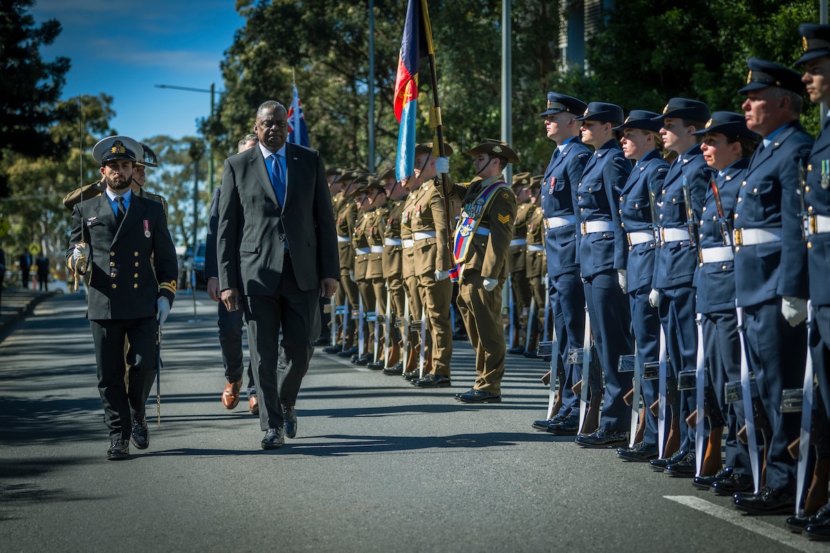 A man in a suit walks down a row of uniformed military personnel.
