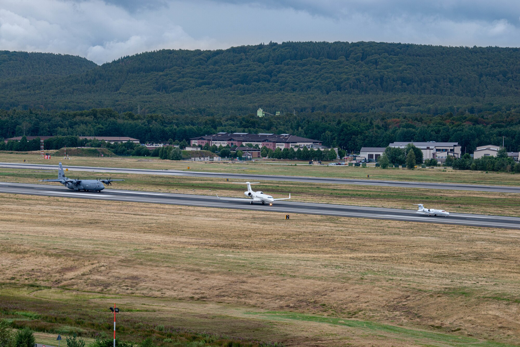 A C-130J Super Hercules aircraft, a C-37A aircraft, and a C-21A aircraft, park on the runway before a scheduled formation flight