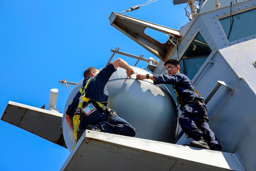 Two sailor perform maintenance on an antenna.