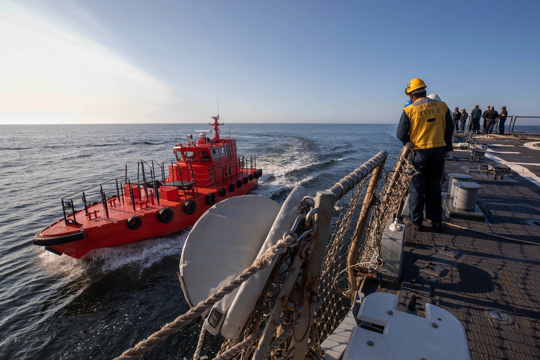 A  small boat pulls up alongside a destroyer.