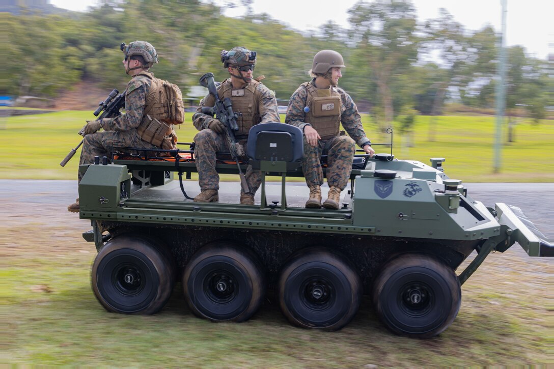 Marines and sailors ride on top of a vehicle.