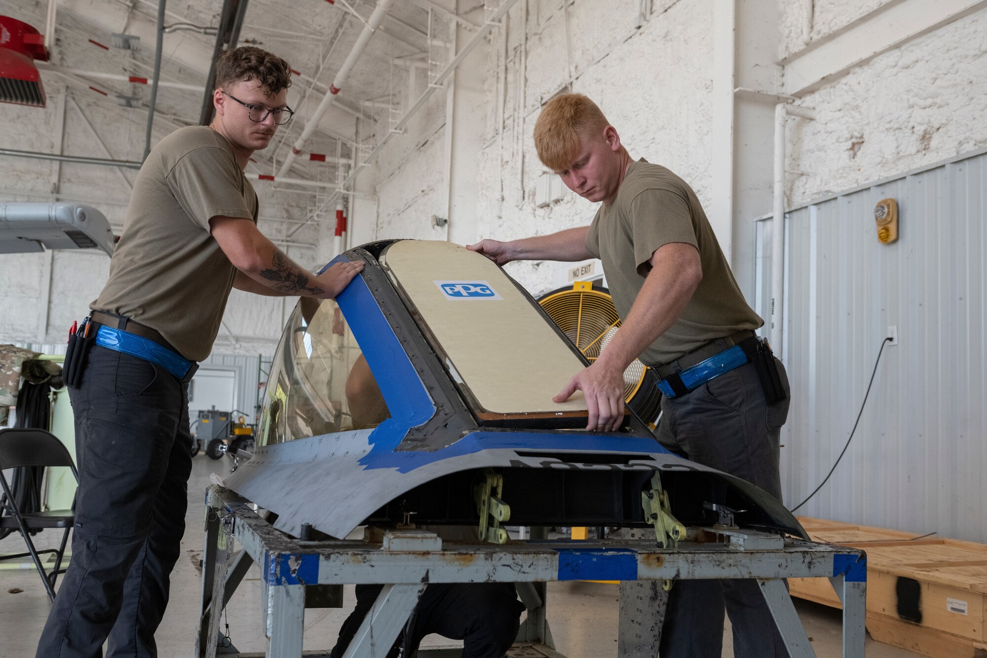 Two people placing a window into a frame of an aircraft hood.