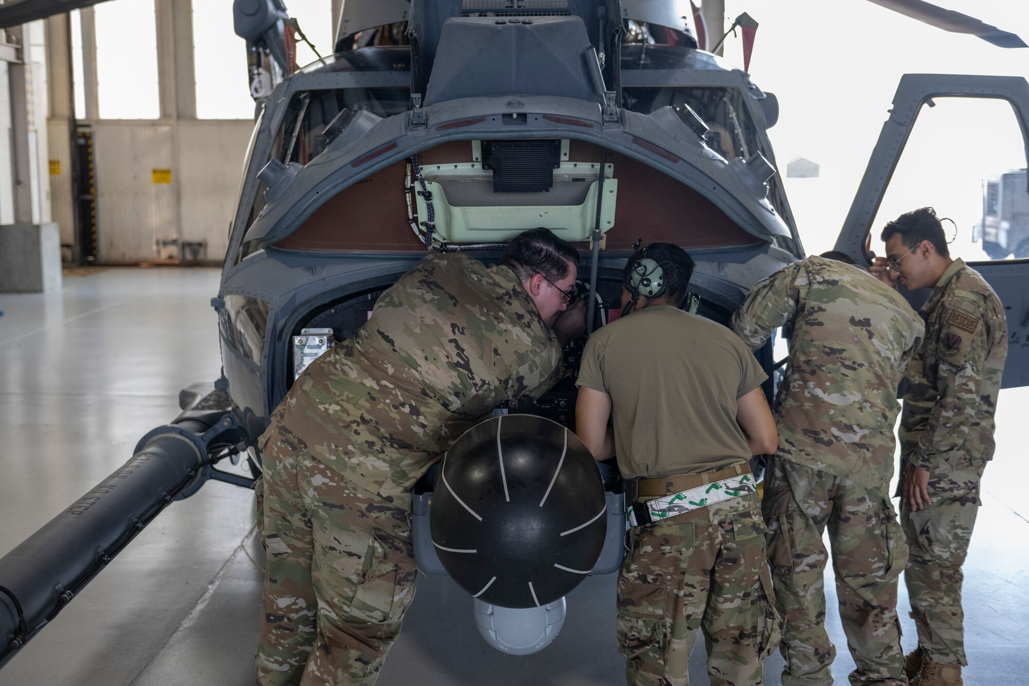 Four people standing at the front of a helicopter leaning over the front piece, inspecting the inside under the hood.