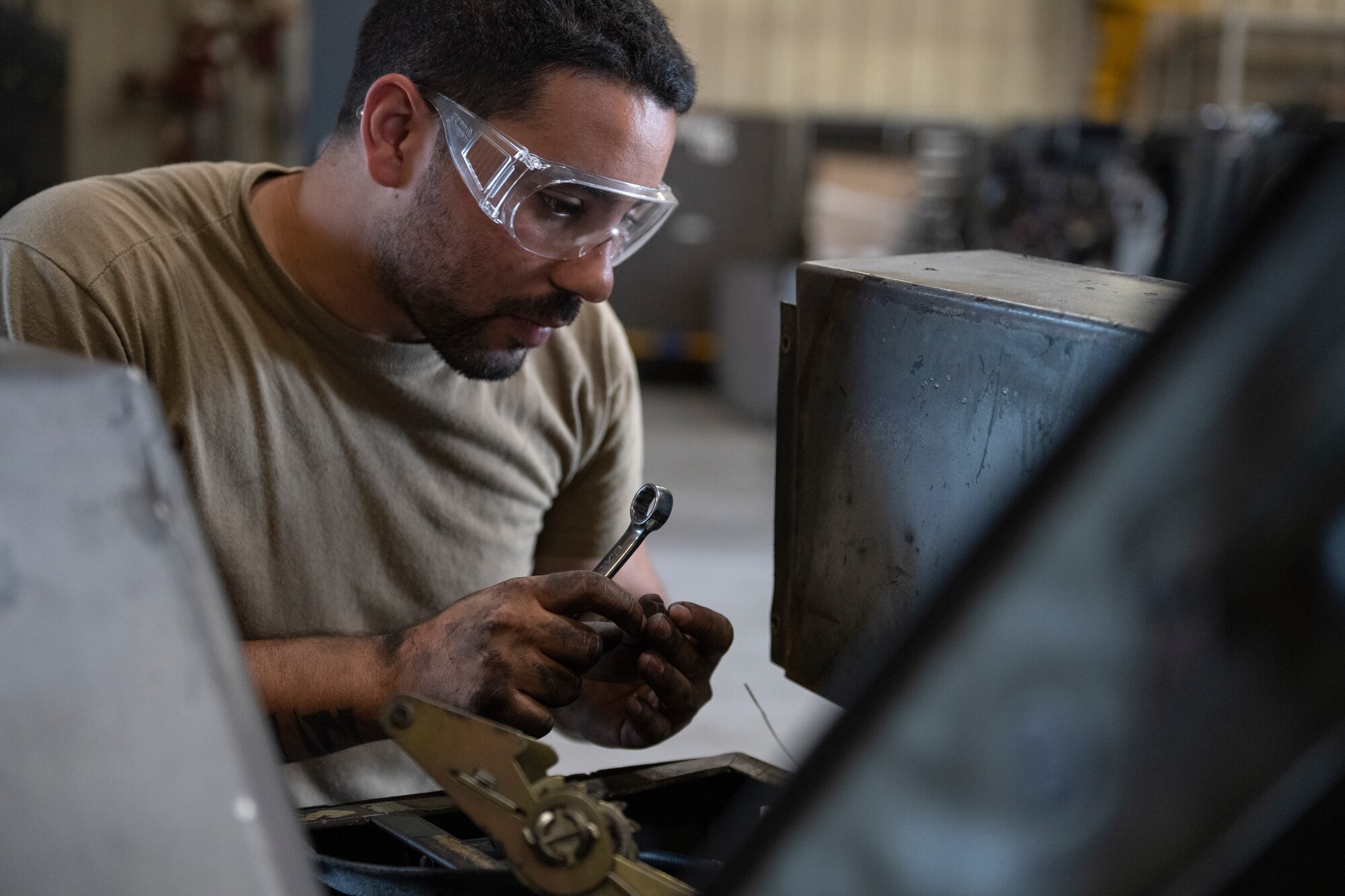 A man wearing clear safety goggles holding a wrench in his hands.