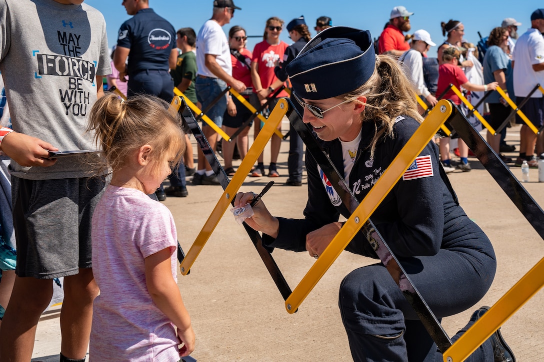 An airman gives a child a small gift as others stand in the background.