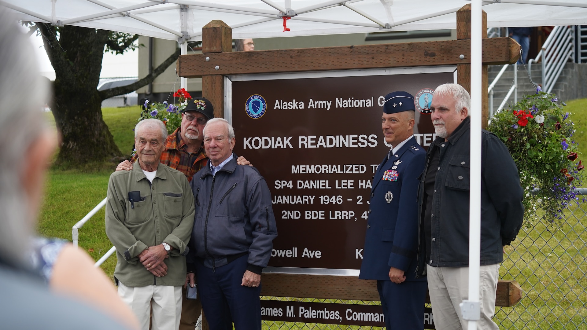 Maj. Gen. Torrence Saxe, adjutant general of 
the Alaska National Guard and commissioner 
of the Department of Military and Veterans 
Affairs, stands with friends and brothers in 
arms of Specialist Four Harmon in front of the 
new Kodiak Reediness Center sign July 27, 
2023, in Kodiak, Alaska.