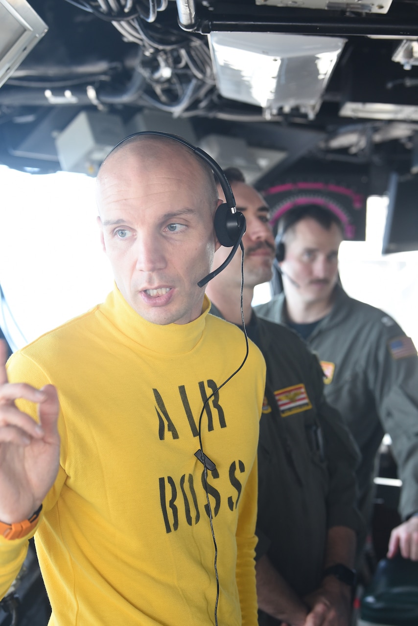 Sailors stand inside a small space.