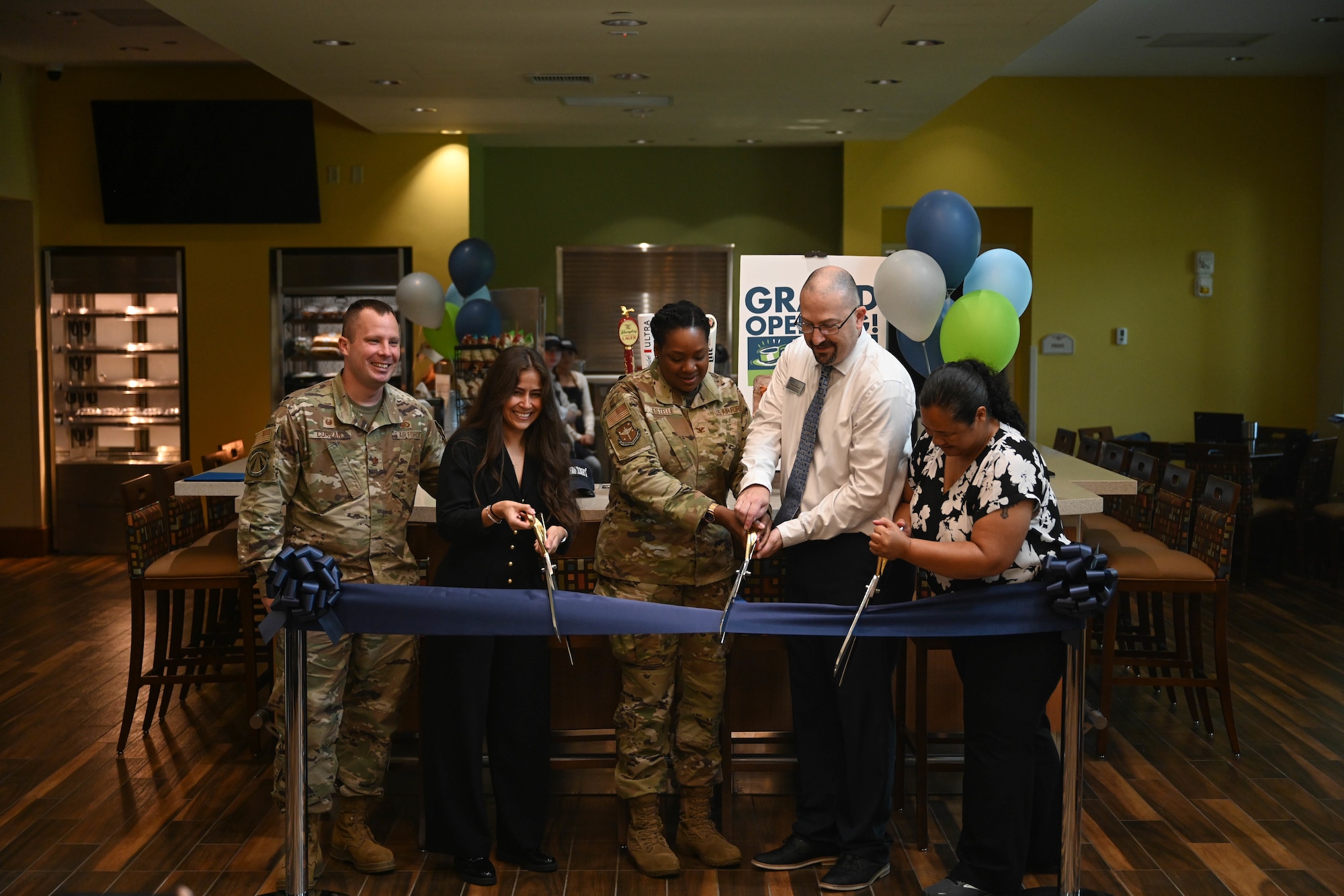 A group of people cut a ribbon in front of a cafe