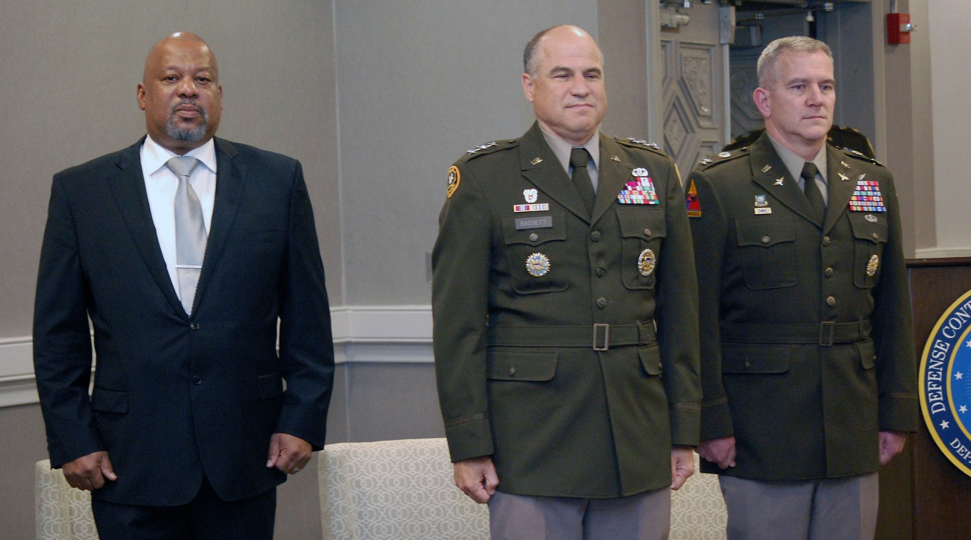One man wears a dark suit while the other two men wear formal Army uniforms
