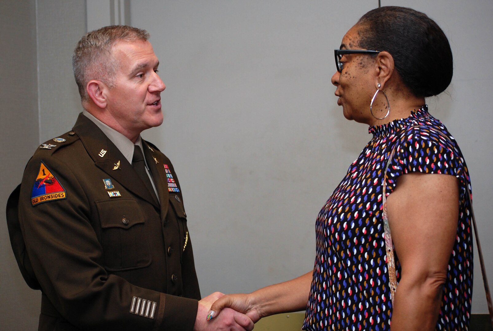 A man in his Army uniform shakes the hand of a woman wearing a multi-colored blouse