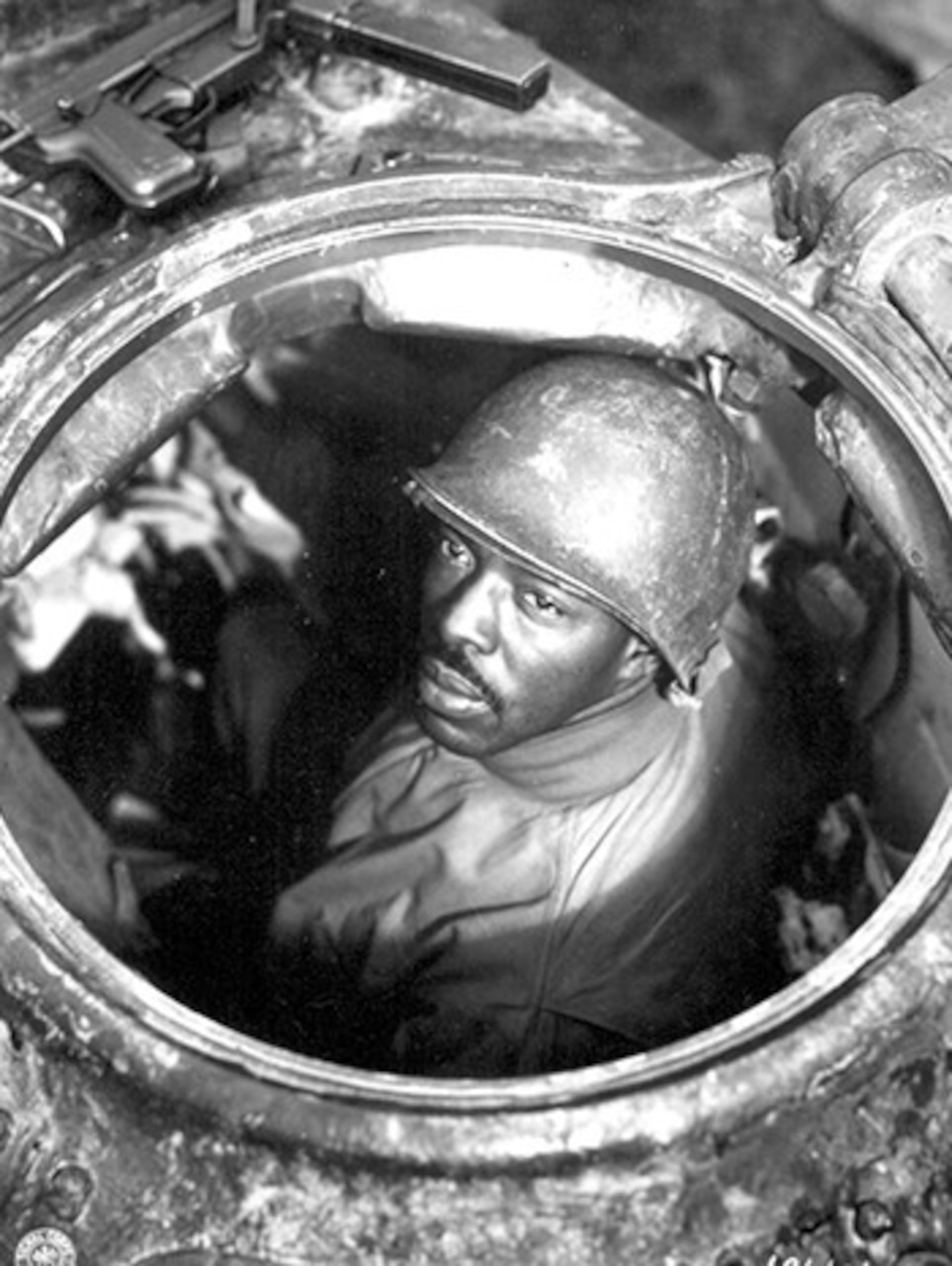 A man looks up from inside the open hatch of a tank.