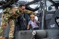 U.S. Army Sgt. Miguel Fonseca, an AH-64 attack helicopter repairer, assigned to the 12th Combat Aviation Brigade, helps a military child explore the inside of an AH-64D Apache longbow helicopter during an event for the Month of the Military Child hosted by the Child Youth Services at USAG Ansbach, Germany, April 27, 2023. April is the Month of the Military Child, which recognizes and honors military children's role in the armed forces community. (U.S. Army Photo by Staff. Sgt. Preston B. Malizia)