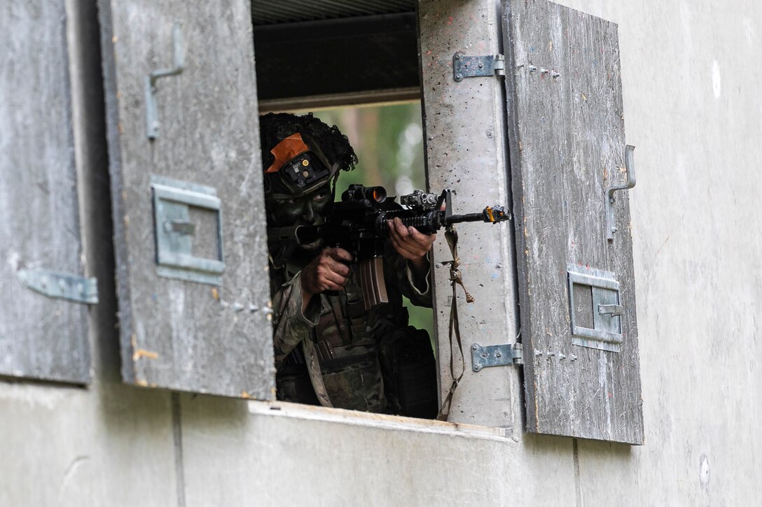 A soldier holds a weapon and fires through a window.