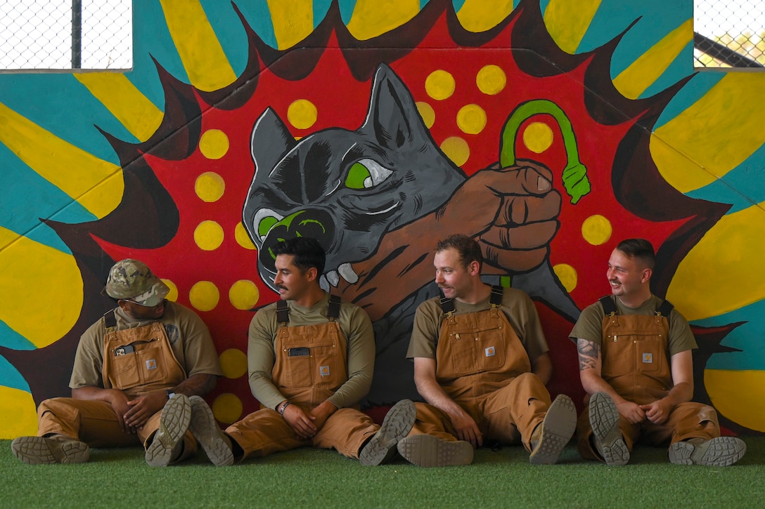 Four service members sit together in front of a mural.