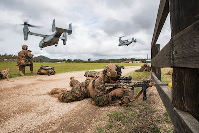Soldiers with weapons hunker on the ground while aircraft fly overhead