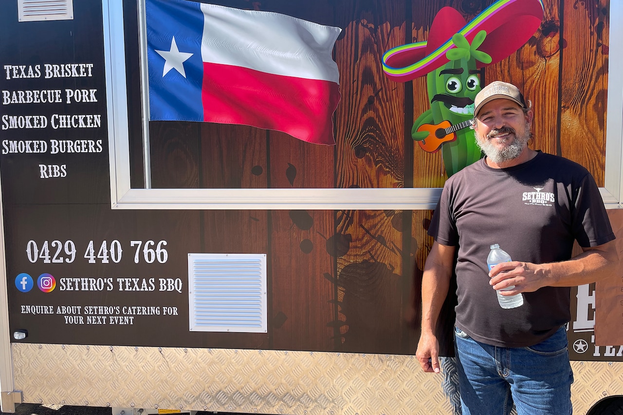A person holding a bottle of water stands in front of a food truck bearing the state flag of Texas.