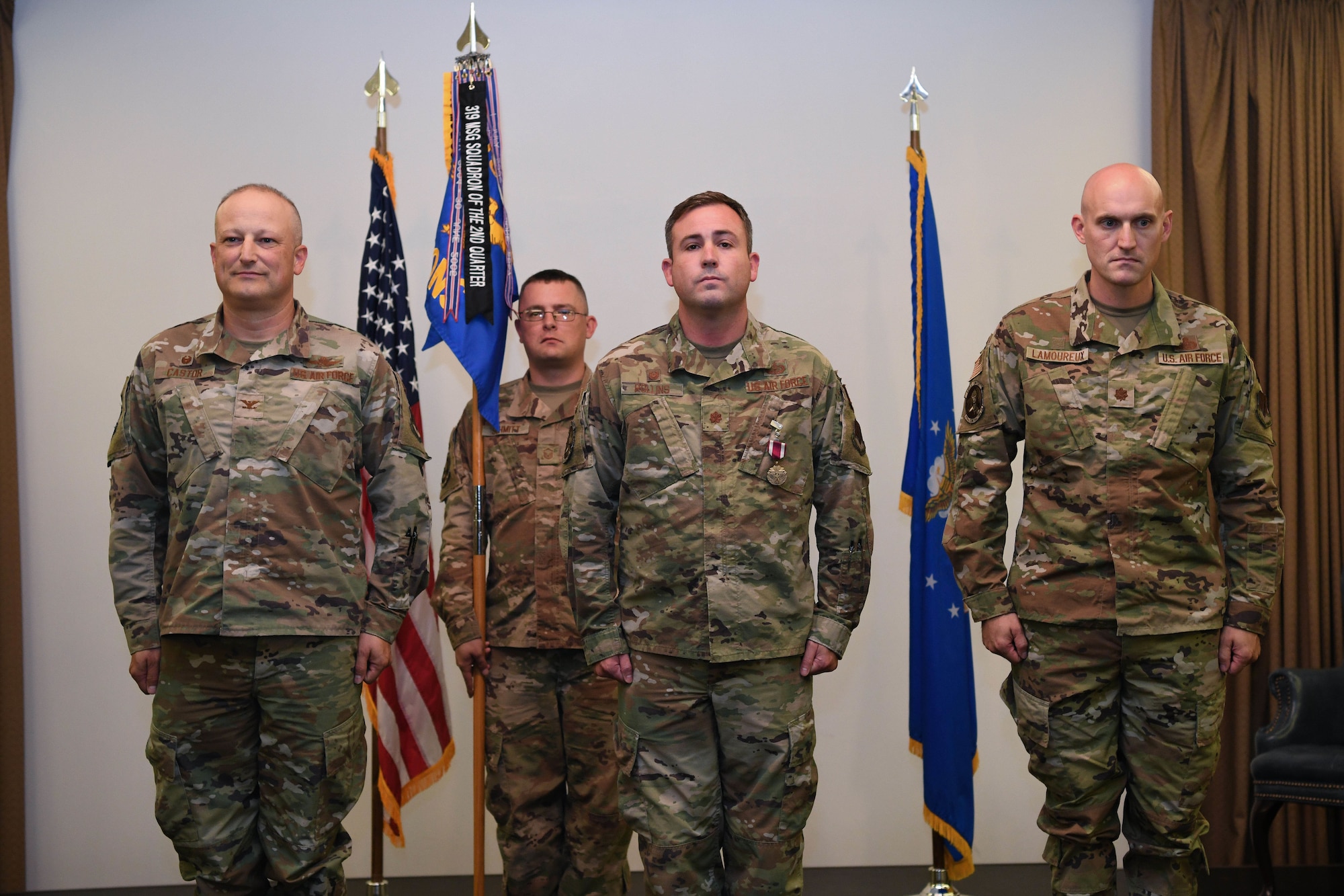 Three men in green military uniforms stand at attention.