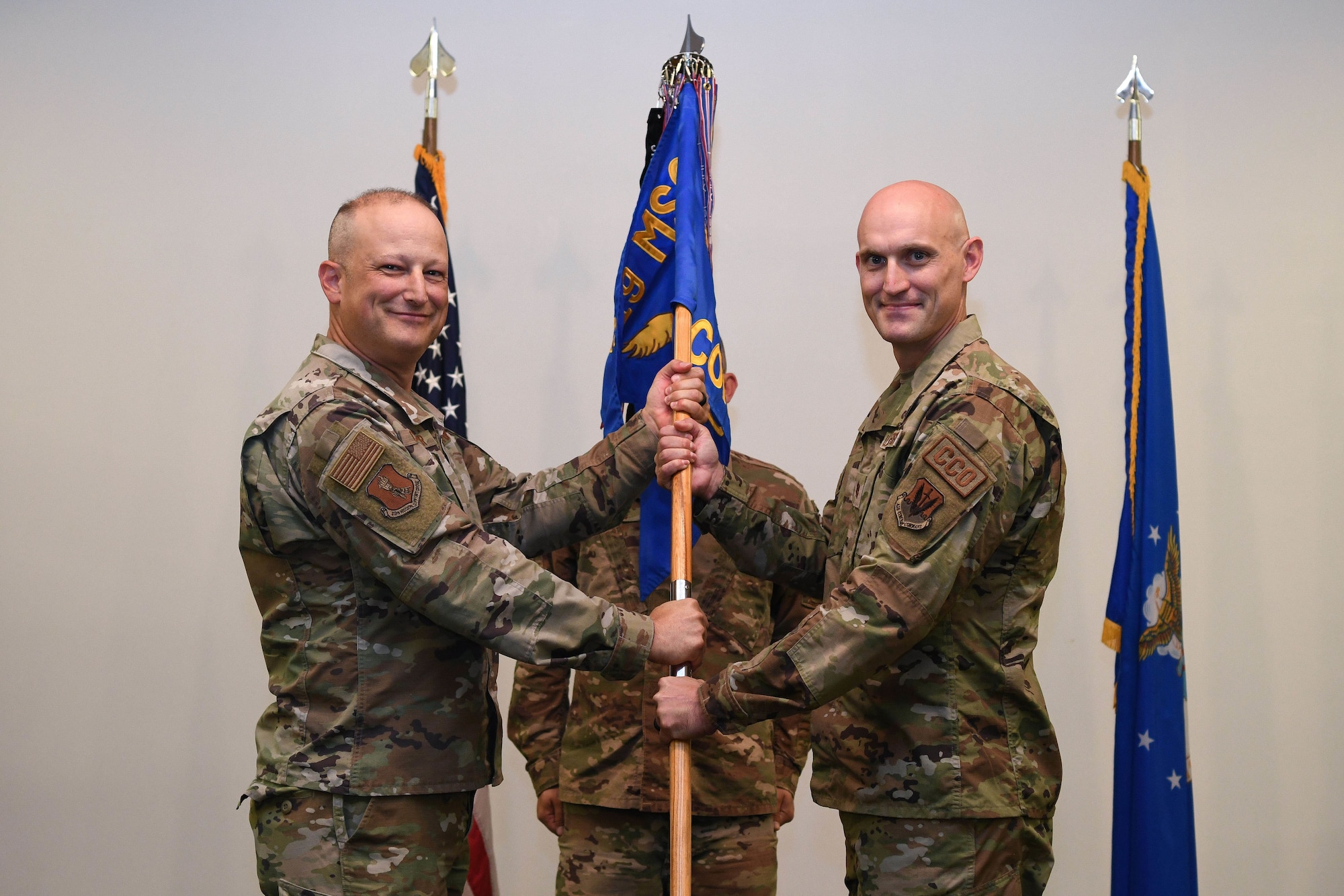 Two men in green military uniforms hold flag.