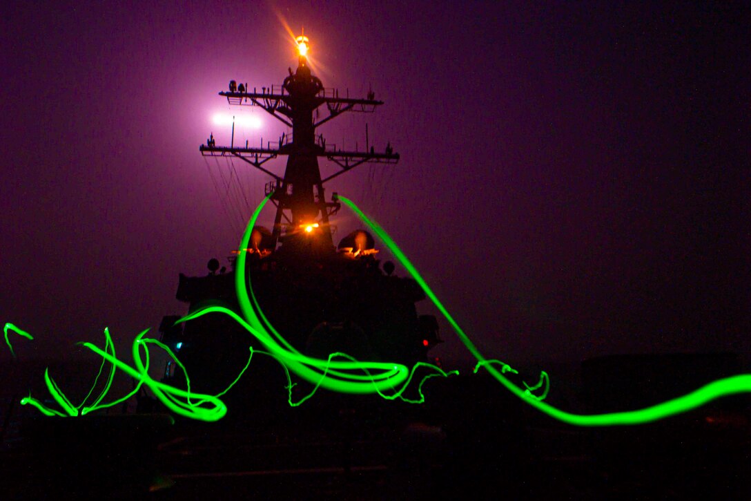 Green streaks of light surround the deck of a ship at night.