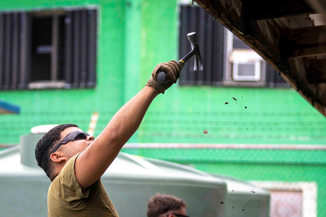 A Marine uses a hammer on the gutters of a building.