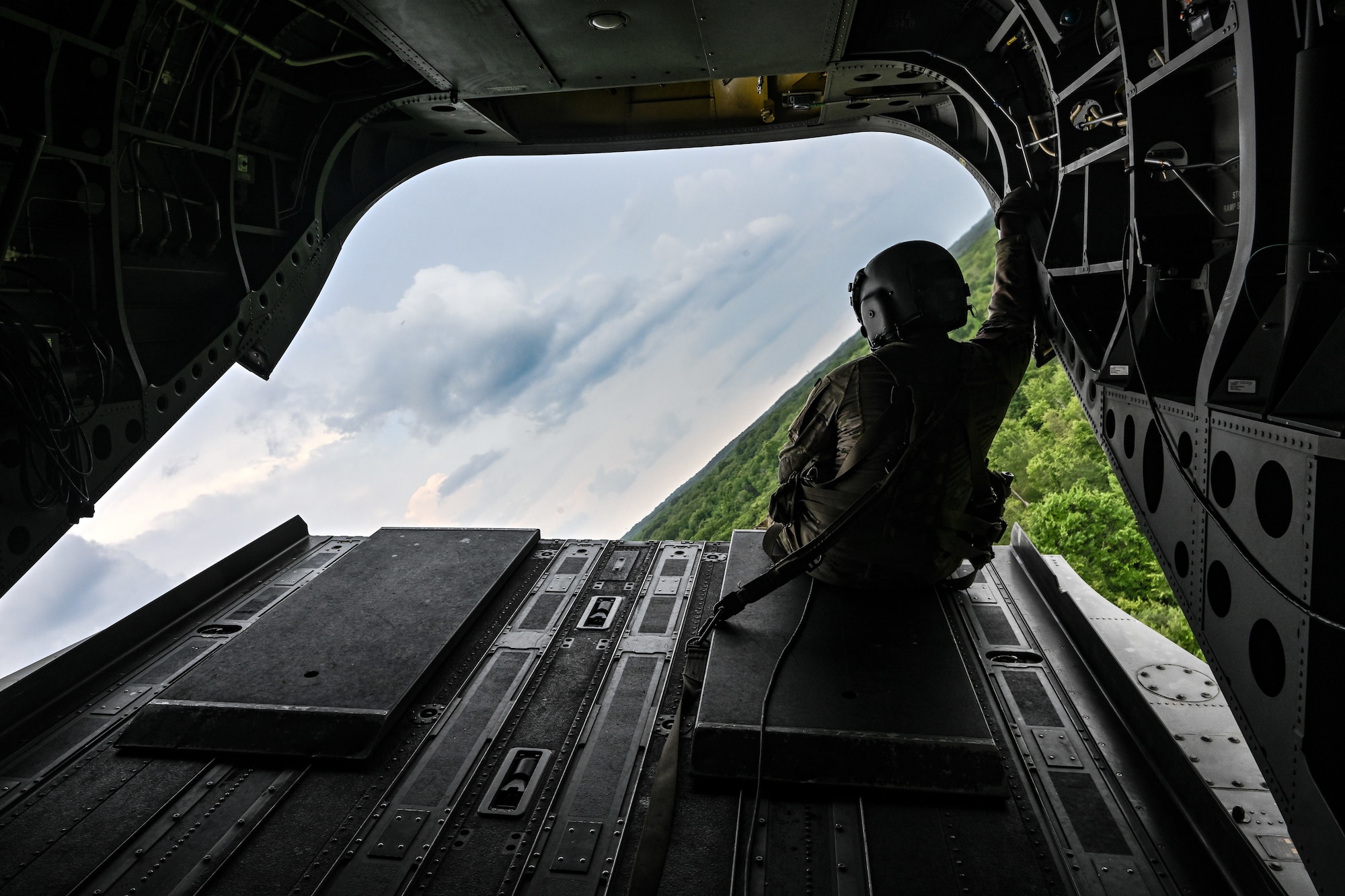 An Ohio National Guard aircrew member sits on the ramp door of a CH-47 Chinook helicopter on July 25, 2023, while flying over Camp James A. Garfield Joint Military Training Center, Ohio.
