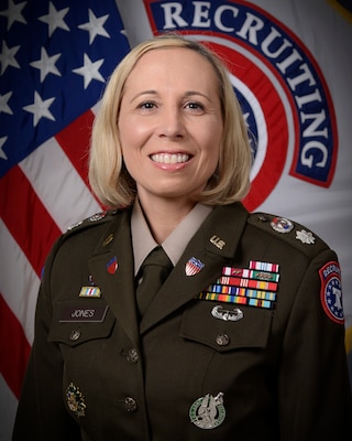 woman wearing army uniform standing in front of two flags.