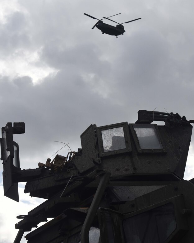 A military helicopter hovers over another military vehicle.