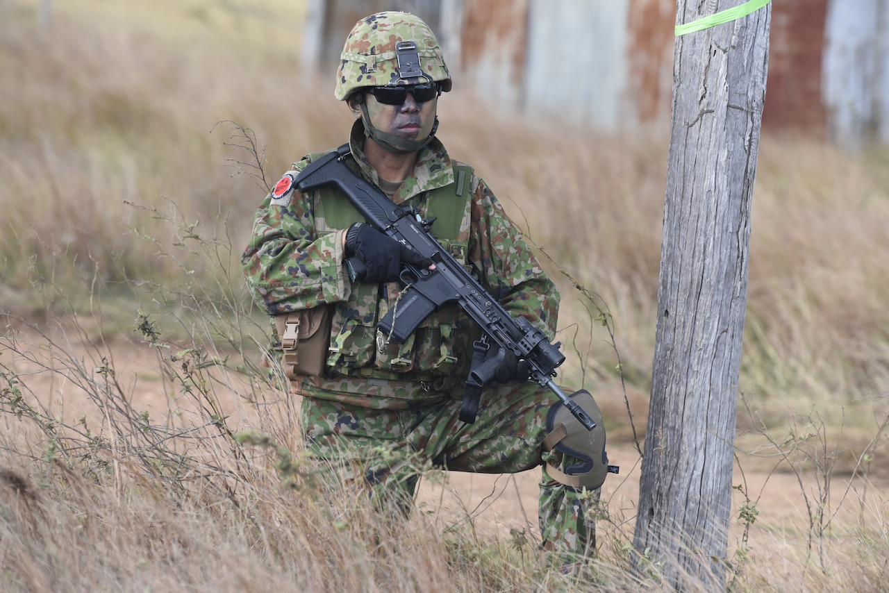 A foreign uniformed service member holds a weapon while kneeling.