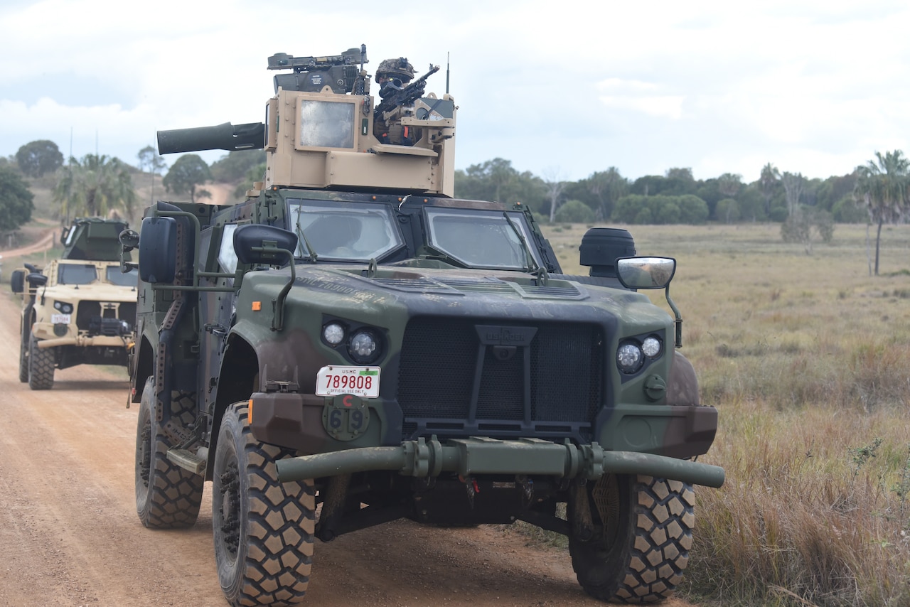 Military vehicles drive down a dirt path.