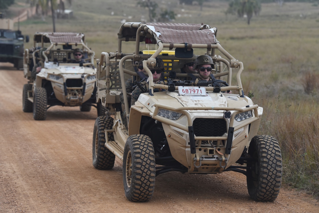 Military vehicles drive down a dirt path.