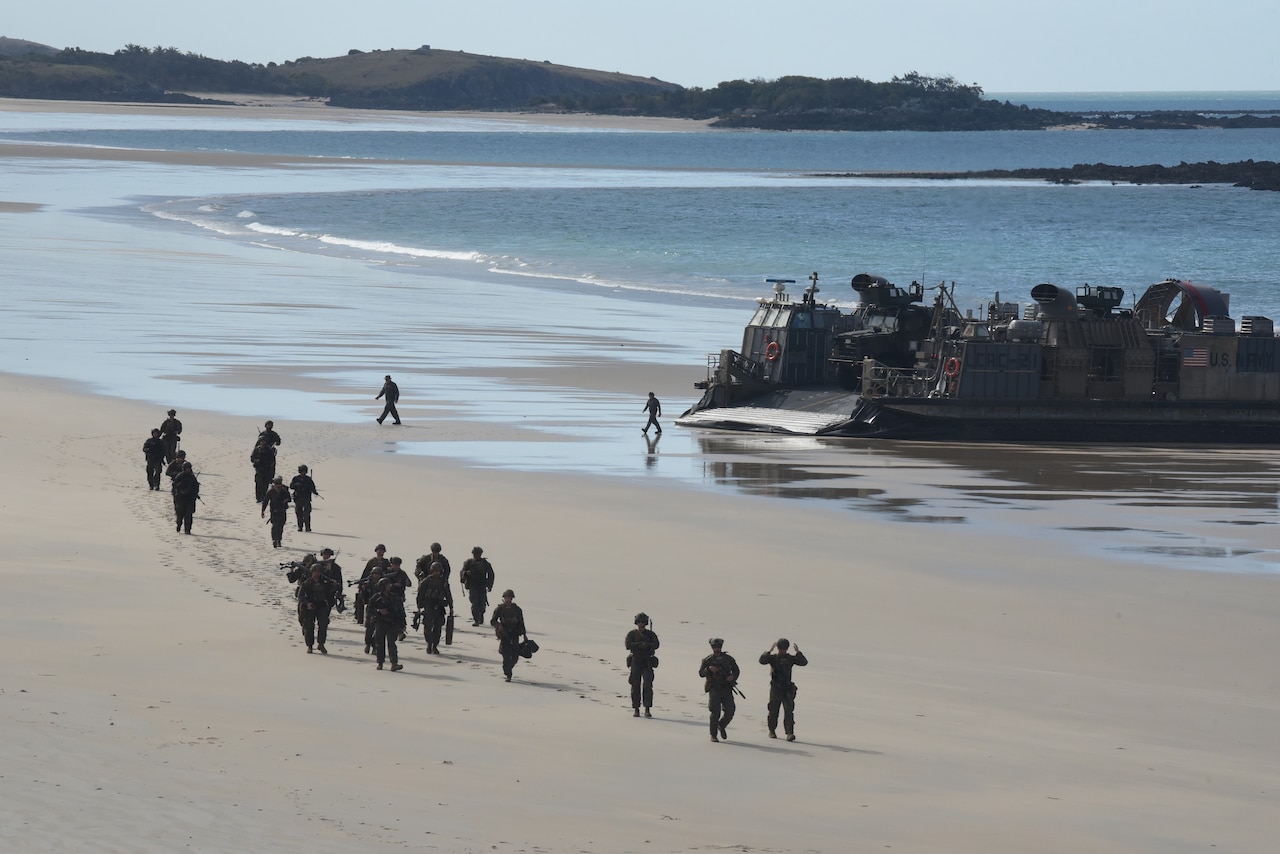 Uniformed service members exit a landing craft that just landed ashore.