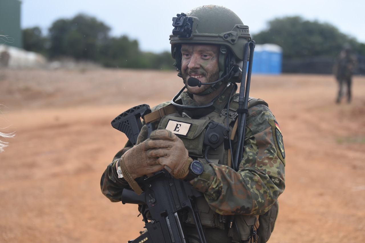 A uniformed service member smiles while holding his weapon.