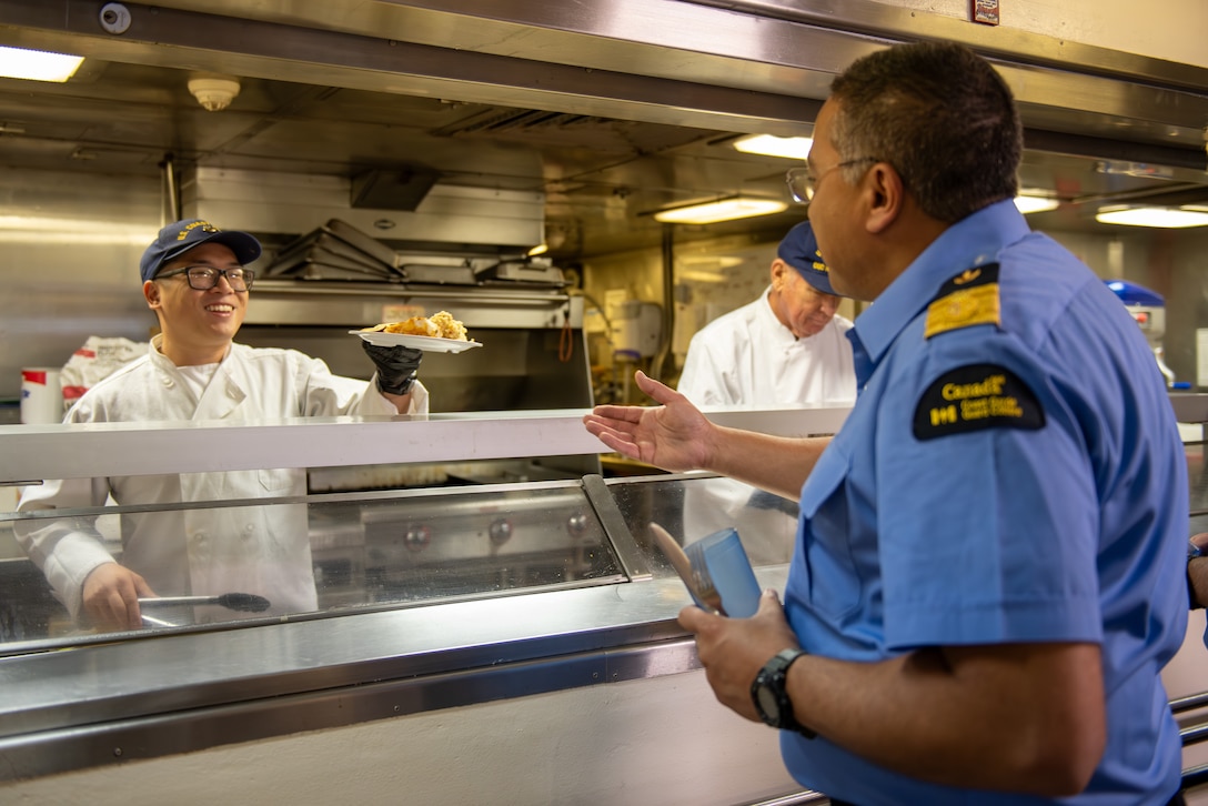 Petty Officer 2nd Class Shannon Ho, a culinary specialist temporarily assigned aboard Coast Guard Cutter Healy (WAGB 20), serves lunch to Youssef Mani, Assistant Commissioner of the Canadian Coast Guard, Arctic Region, while underway in the Beaufort Sea, July 28, 2023. The crew conducted a passenger exchange with the Canadian Coast Guard Ship Sir Wilfrid Laurier and crew off the coast of Utqiagvik, Alaska. (Coast Guard photo by Petty Officer 3rd Class Briana Carter)