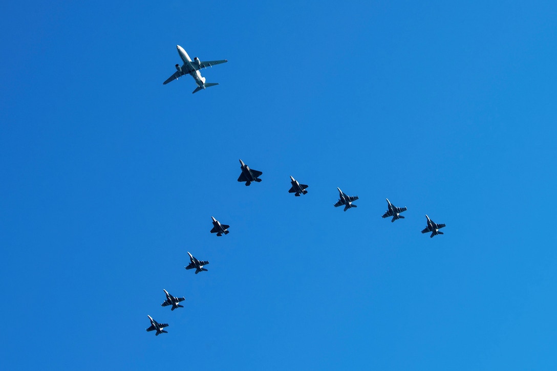U.S. and Australian aircraft fly in a triangular motion behind a larger aircraft as seen from below.