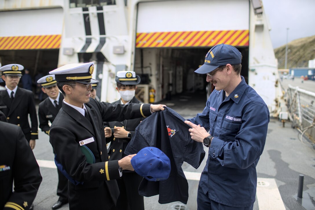 H. Takahashi, ENS Japan Maritime Self Defense Force, and U.S. Coast Guard Petty Officer 2nd Class Derek Mazzocoli make a clothing trade, swapping uniform items while on the flight deck of Coast Guard Cutter Bertholf (WMSL 750) moored in Dutch Harbor, Alaska, June 5, 2023. The ships crews built upon and shaped partnerships. (U.S. Coast Guard photo by Lt. Cmdr. Scott Mccann)