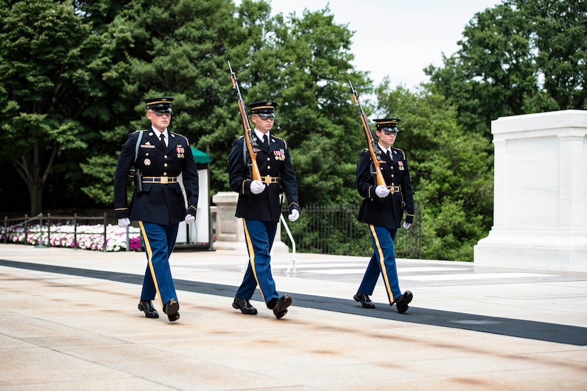 Three soldiers, two carrying rifles, march past the Tomb of the Unknown  Soldier.