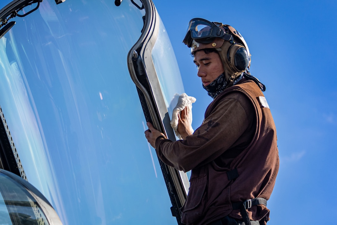 A sailor wipes the window of a large fighter jet.