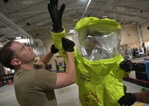 Firefighters responding to a simulated hazardous materials spill are assisted with putting on protective suits.