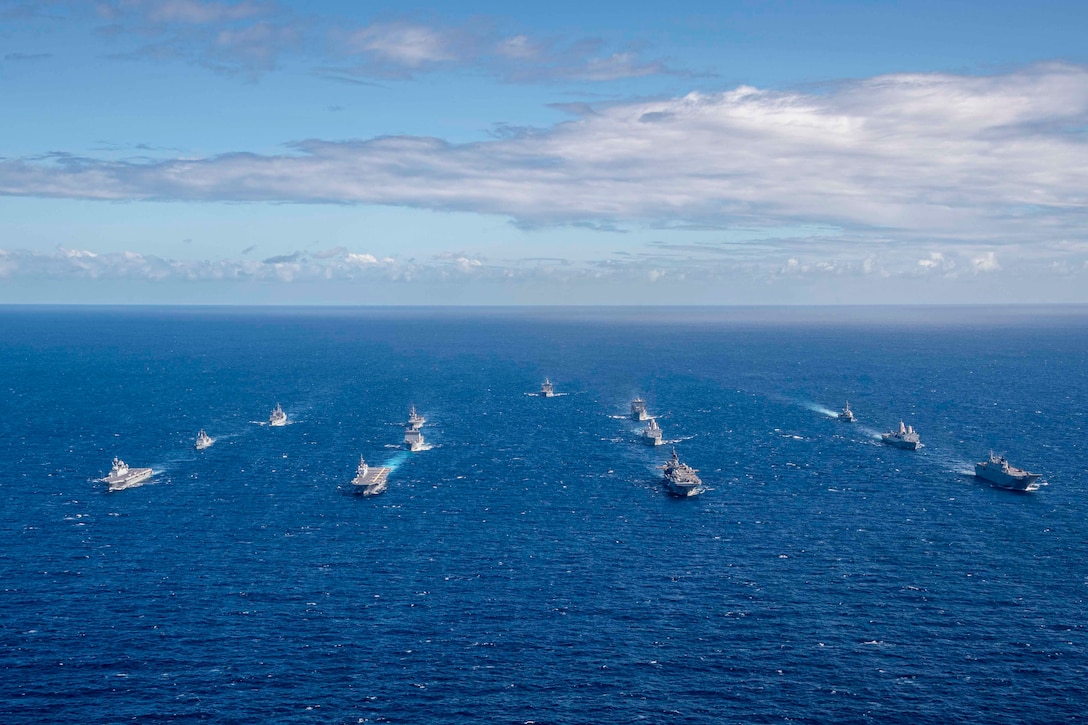 Thirteen ships travel through a body of water in formation.