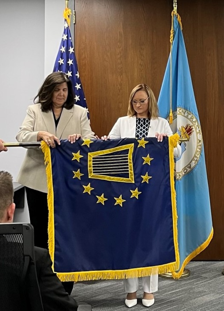 two women in business attire unfurl a flag