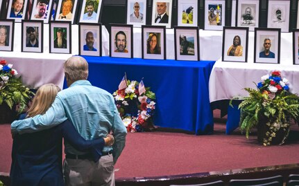 Two people embrace as they look at photos of coworkers who have passed away.