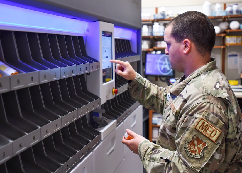 A man in uniform presses buttons on a machine that fills prescriptions.