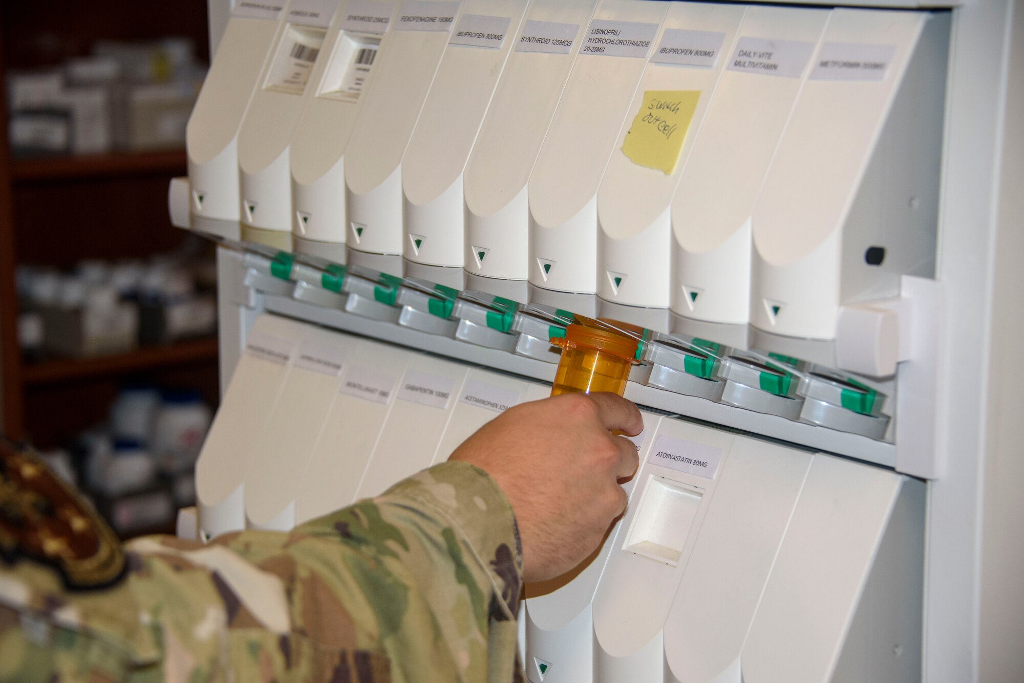 A military member in uniform holds a pill bottle to a machine.