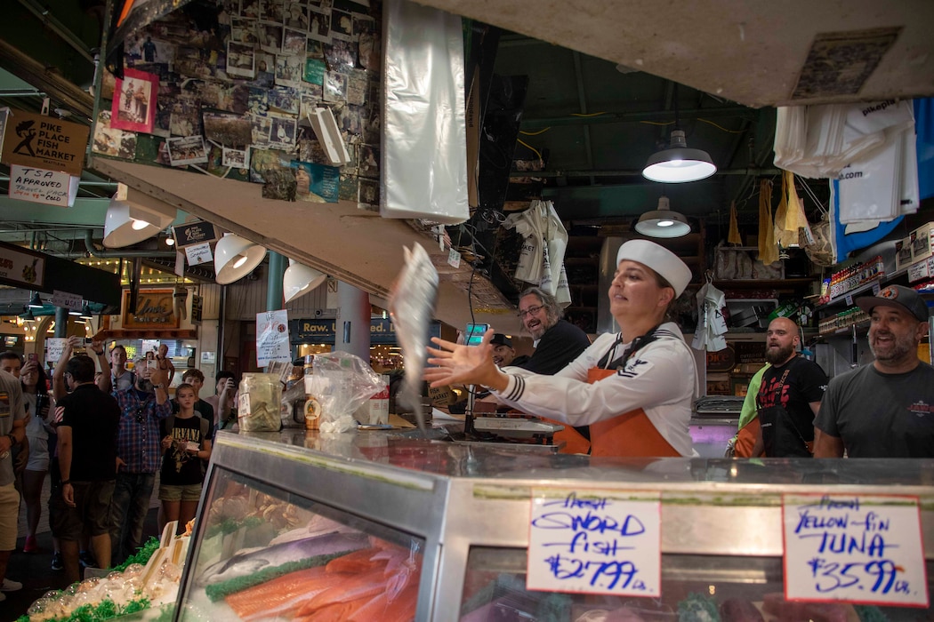 230802-N-NR998-1035 SEATTLE (Aug. 2, 2023) Mass Communication Specialist 2nd Class Madison Cassidy, from Inverness, Fla., catches fish during a visit with Sailors to Pike Place Market during Seattle Fleet Week, Aug. 2, 2023. Seattle Fleet Week is a time-honored celebration of the sea services and provides an opportunity for the citizens of Washington to meet Sailors, Marines and Coast Guardsmen, as well as witness firsthand the latest capabilities of today’s U.S. and Canadian maritime services. (U.S. Navy photo by Chief Mass Communication Specialist Gretchen M. Albrecht)