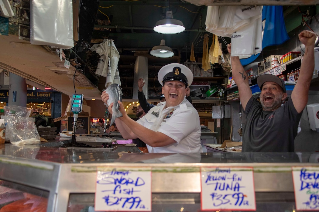 230802-N-YF131-1056 SEATTLE (Aug. 2, 2023) Chief Mass Communication Specialist Gretchen Albrecht, from Chino Hills, Calif., catches fish with Sailors at Pike Place Market during Seattle Fleet Week, Aug. 2, 2023. Seattle Fleet Week is a time-honored celebration of the sea services and provides an opportunity for the citizens of Washington to meet Sailors, Marines and Coast Guardsmen, as well as witness firsthand the latest capabilities of today’s U.S. and Canadian maritime services. (U.S. Navy photo by Mass Communication Specialist 2nd Class Madison Cassidy)