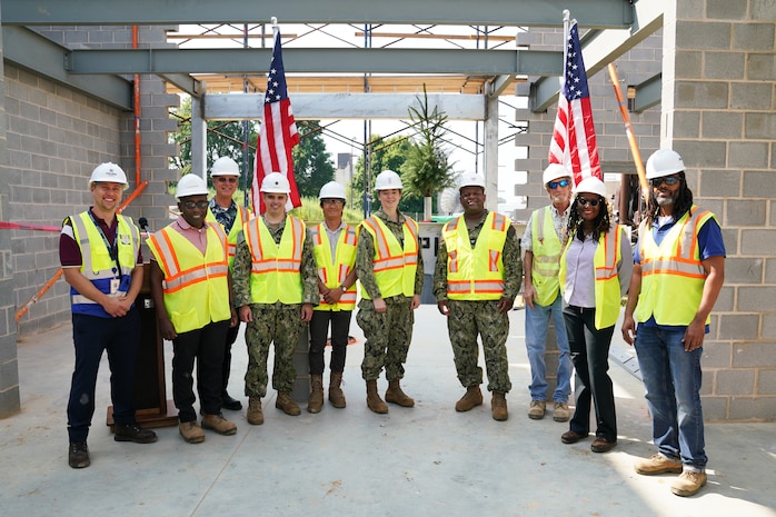 Group of construction personnel stand in front of a steel beam