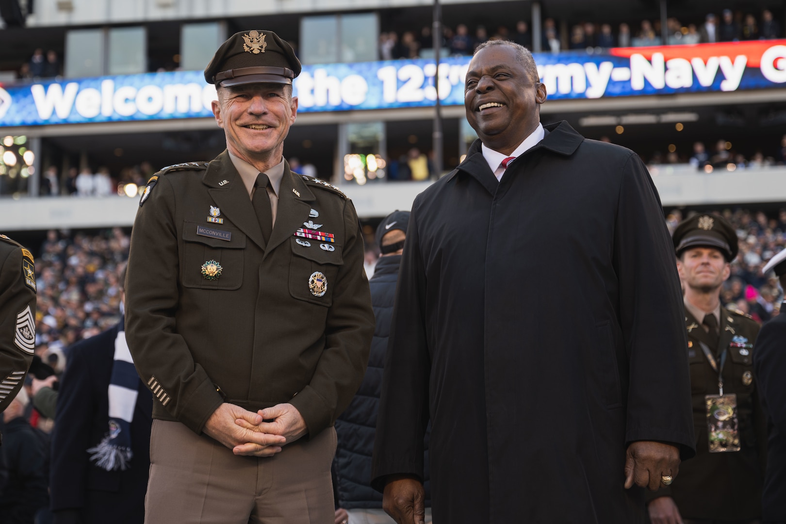 Two men, one dressed in civilian clothing and the other wearing a military uniform, smile broadly.