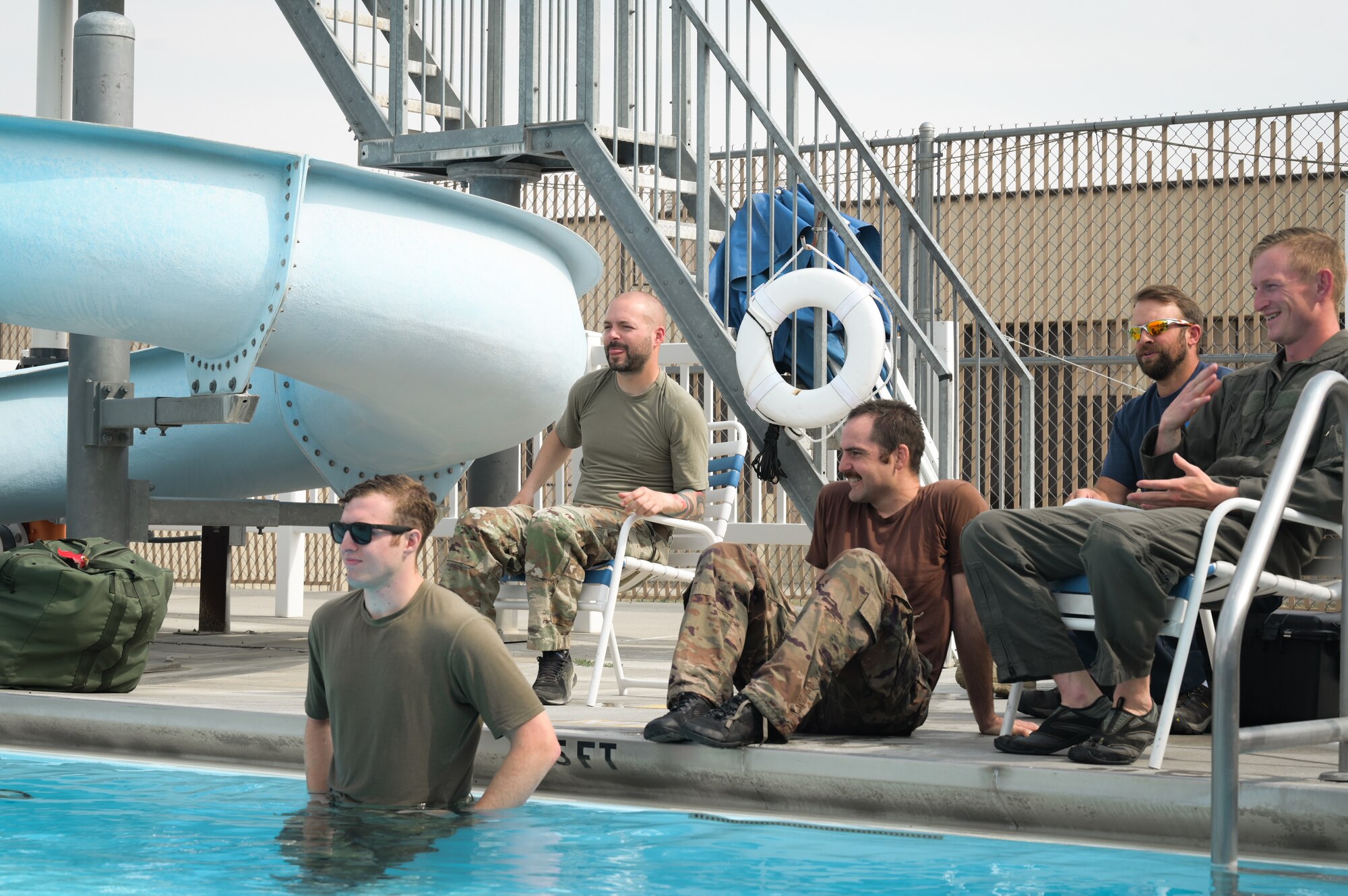 Five men sit near the edge of a pool together.