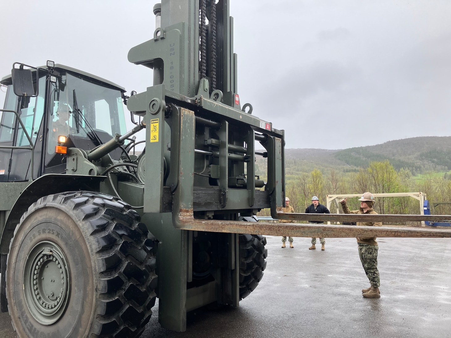 CM1 Curtis Cox and EO2 Gage Bochette observe while EOCA Stephen Cosby operates a 25K Rough Terrain Container Handler and EO2 Tyler Campbell ground guides.