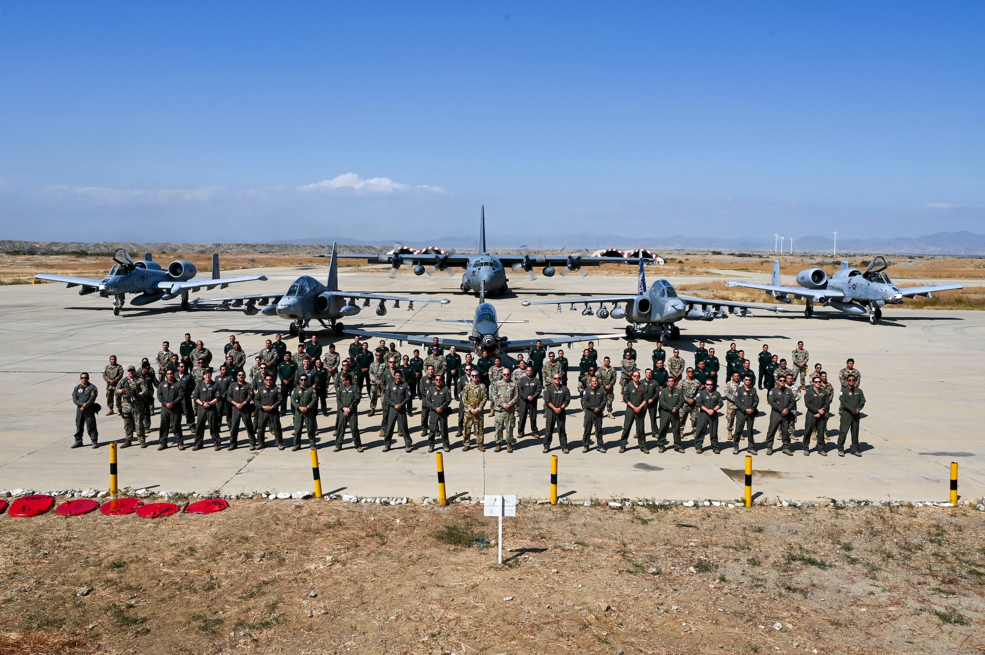 A combined formation of U.S. and Peruvian Airmen stand in front of (front to back) a KT-1 light attack aircraft, two SU-25 attack aircraft, two A-10 attack aircraft, and a C-130 cargo aircraft.
